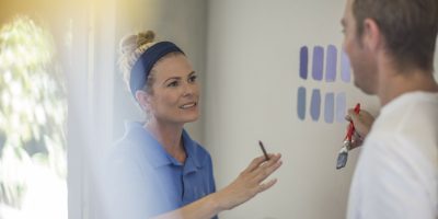 Couple holding brochure discussing paint colours on wall