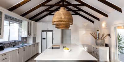 Lighting equipment hanging in a row from mansard roof over kitchen island in modern kitchen. Copy space, white, unaltered, home and interior decoration concept.