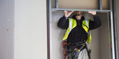 A carpenter in a small space fitting a shelf into a wall cupboard.