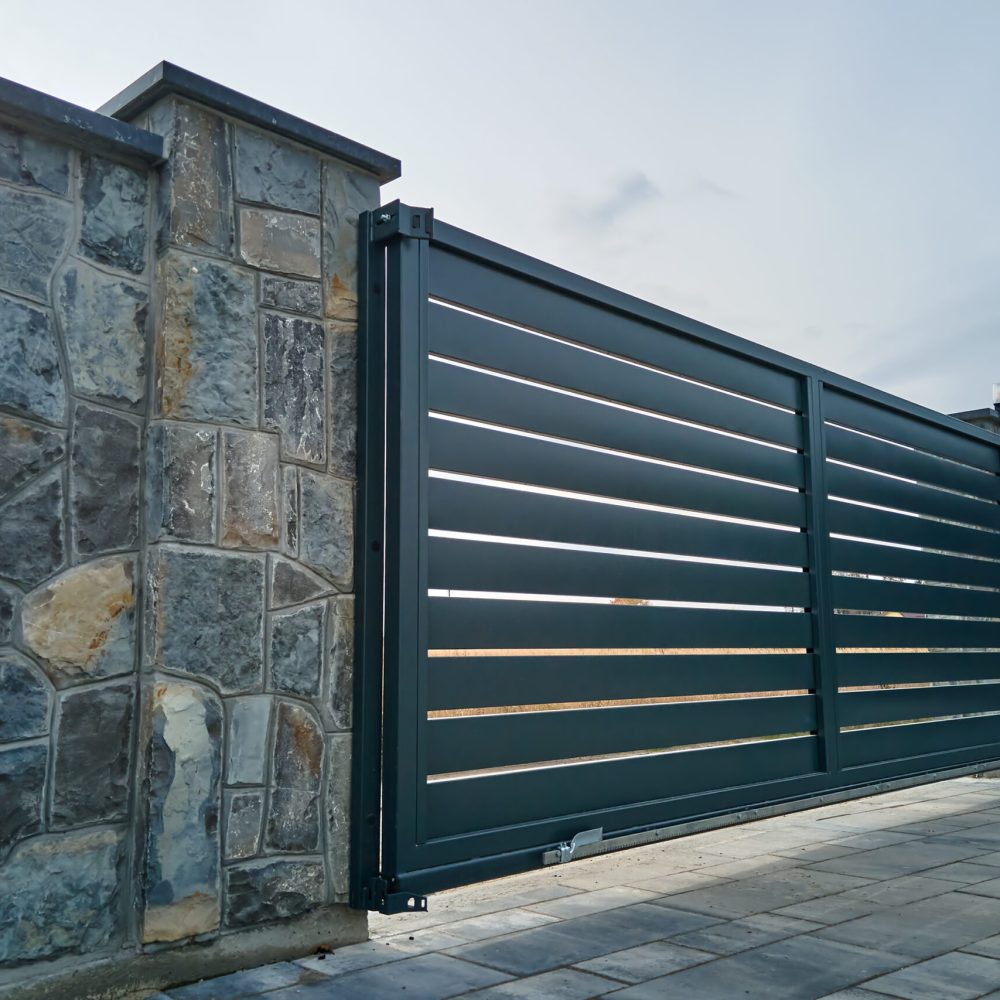 Wide automatic sliding gate with remote control installed in high stone fense wall. Security and protection concept.