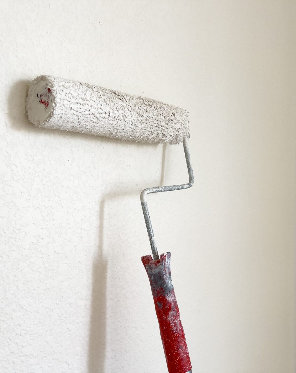 Detailed process of painting a wall, with a focus on a paint roller applying a fresh white coat, symbolizing the transformative power of a simple home improvement task.