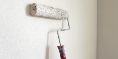 Detailed process of painting a wall, with a focus on a paint roller applying a fresh white coat, symbolizing the transformative power of a simple home improvement task.