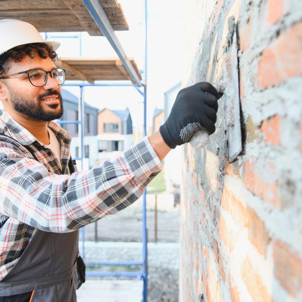 Worker in hard hat plastering brick wall with cement mortar. Building new residential house, skill and craftsmanship