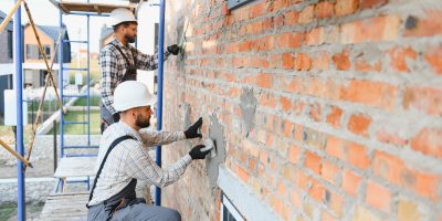 Construction workers applying plaster to a brick wall using a trowel at a renovation site. Building new home